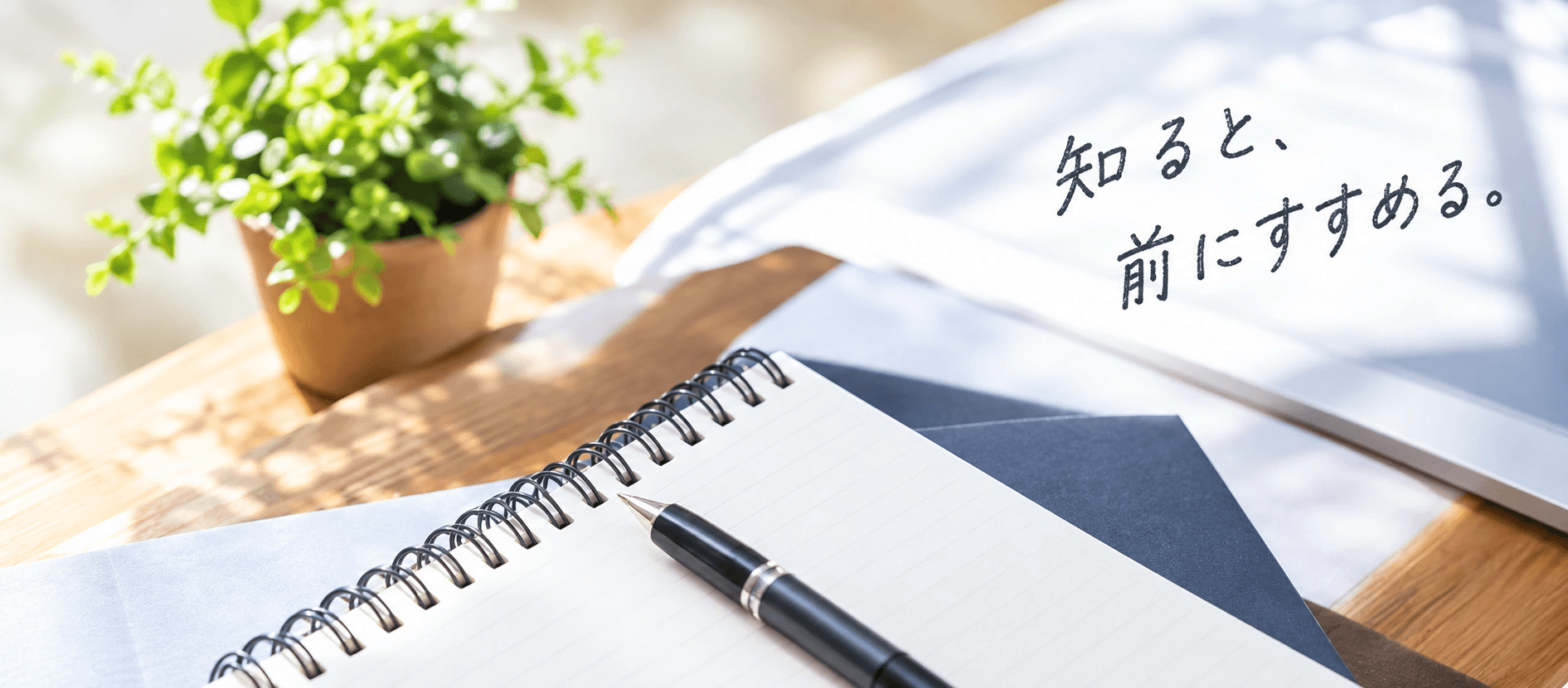 ノートとペンを広げた机。「知ると、前にすすめる。」の手書き装飾。